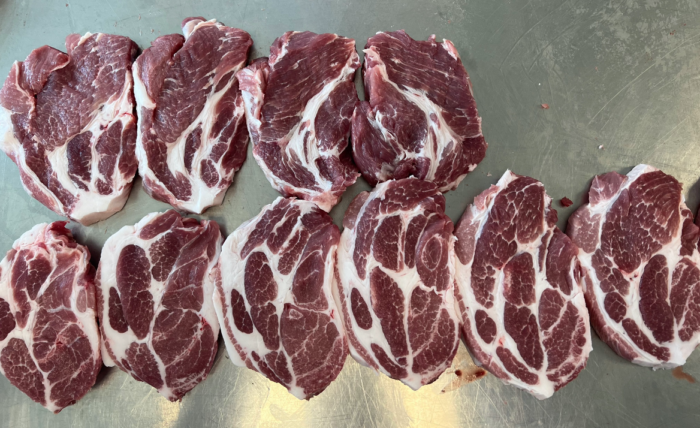 Sliced pork cuts arranged in a row on a stainless steel surface.